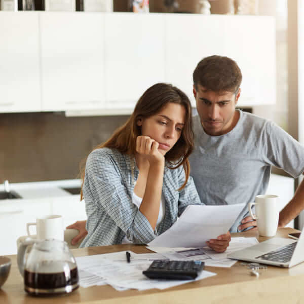 A young couple sitting at their kitchen table, looking concerned while reviewing financial bills to determine if they can get an instant loan in Canada.