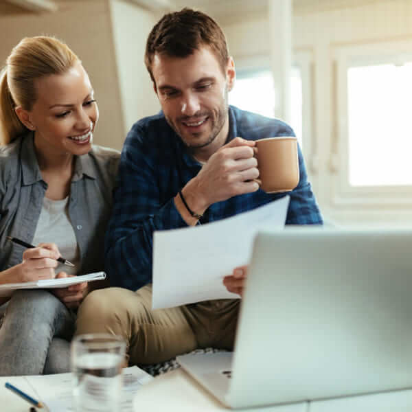 A person holding a smartphone and a credit card while sitting at a desk with a laptop, evaluating loan options based on their borrower profile.
