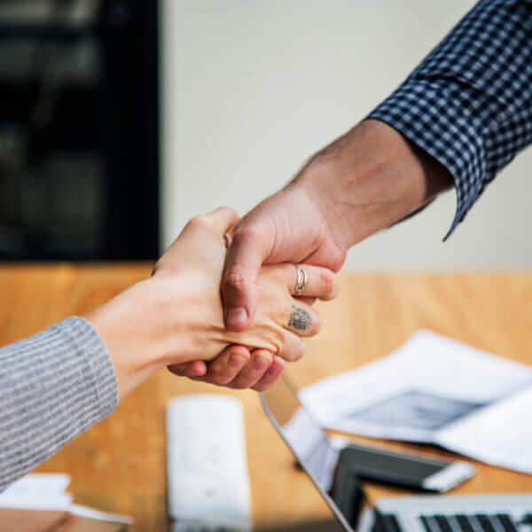 Close-up of a firm handshake over a desk with a laptop, symbolizing a successful agreement before a loan application.